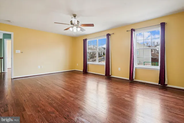 an empty room with wooden floor chandelier fan and windows