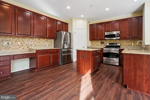 a kitchen with stainless steel appliances wooden floors wooden cabinets a stove a sink and a refrigerator