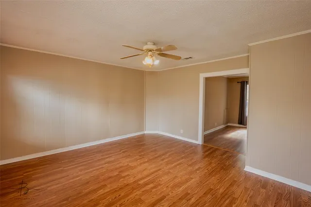 a view of an empty room with wooden floor and a ceiling fan