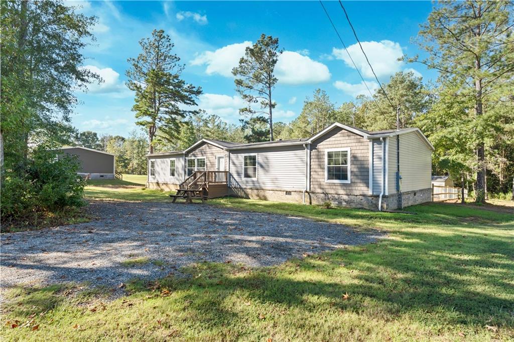 89 Ridge Road Seale, AL 36875 - Photo 2 of 46 Exterior featuring light siding, a gravel drive, natural wood deck, and surrounding mature trees