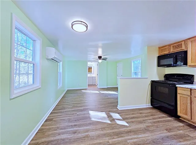 a view of a kitchen and an empty room with wooden floor and a window