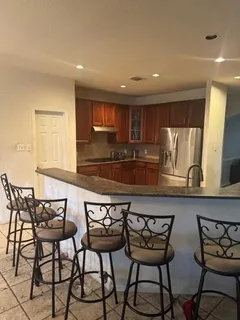 a kitchen with stainless steel appliances kitchen island granite countertop a dining table chairs and a refrigerator