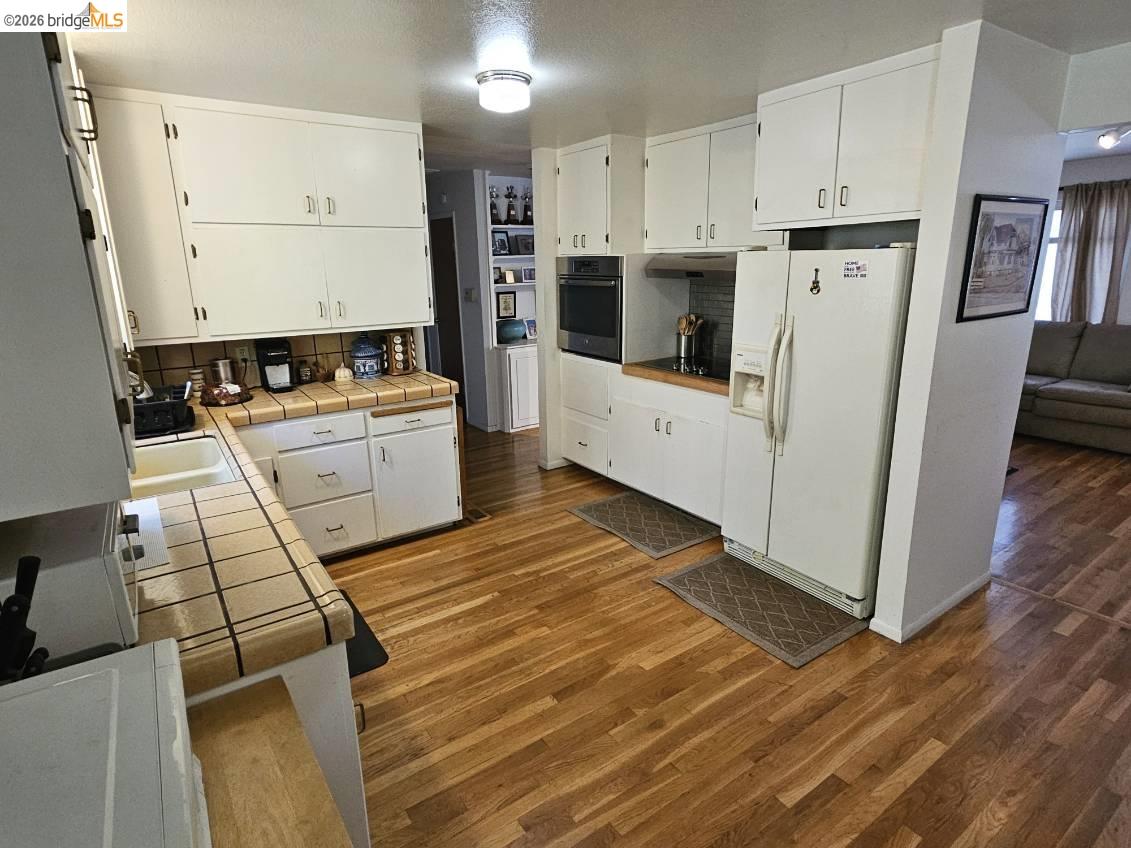 19967 Peaceful Oak Road Sonora, CA 95370 - Photo 8 of 35 Kitchen with tile countertops, white fridge with ice dispenser, white cabinets, and dark wood finished floors