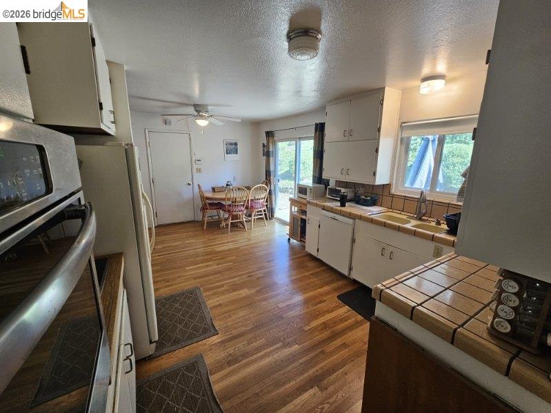 19967 Peaceful Oak Road Sonora, CA 95370 - Photo 10 of 35 Kitchen featuring tile countertops, white cabinetry, stainless steel appliances, dark wood-style floors, and ceiling fan