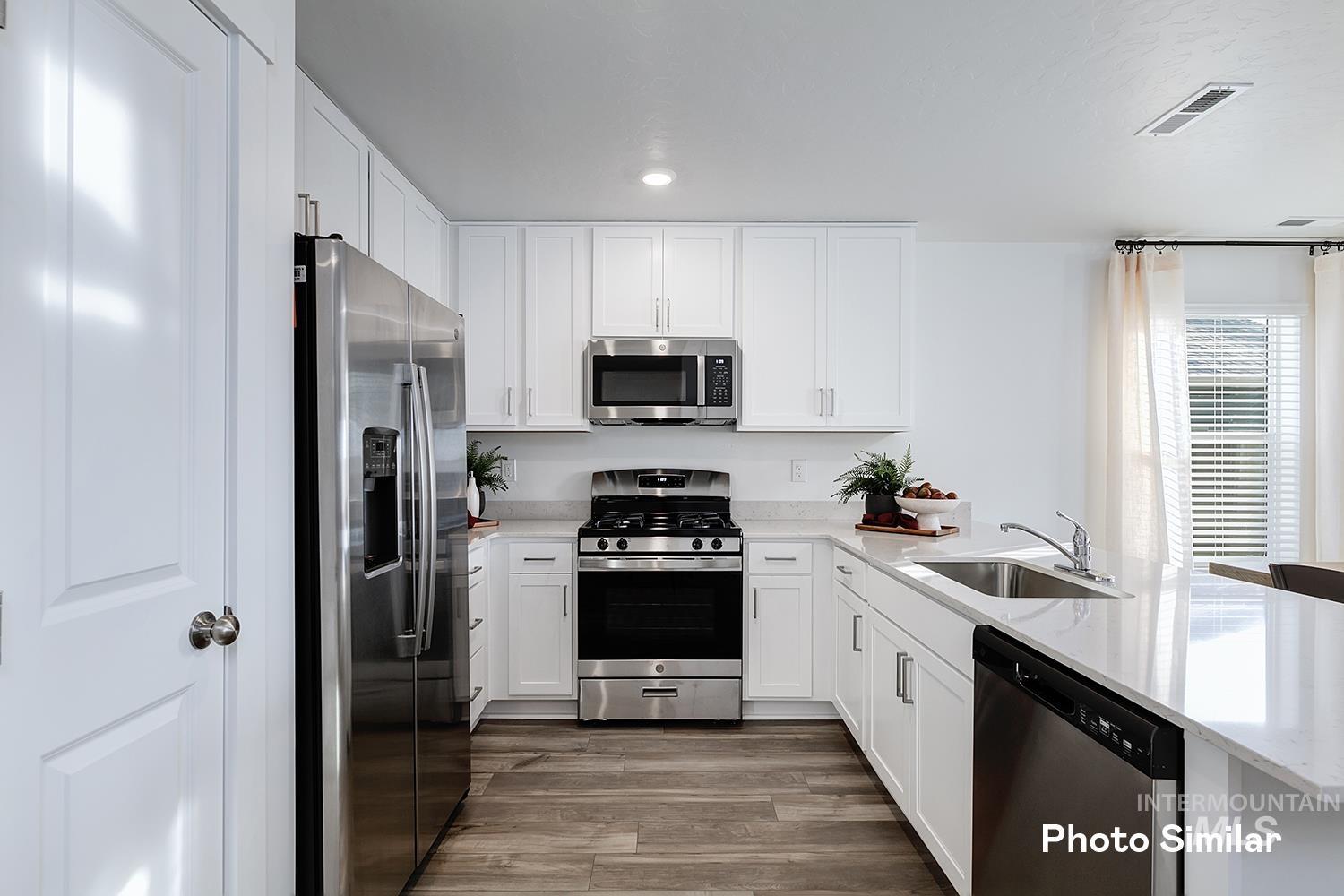 3045 North Kankakee Way Kuna, ID 83634 - Photo 8 of 19 Kitchen featuring appliances with stainless steel finishes, white cabinets, light stone countertops, a peninsula, and light wood-style floors