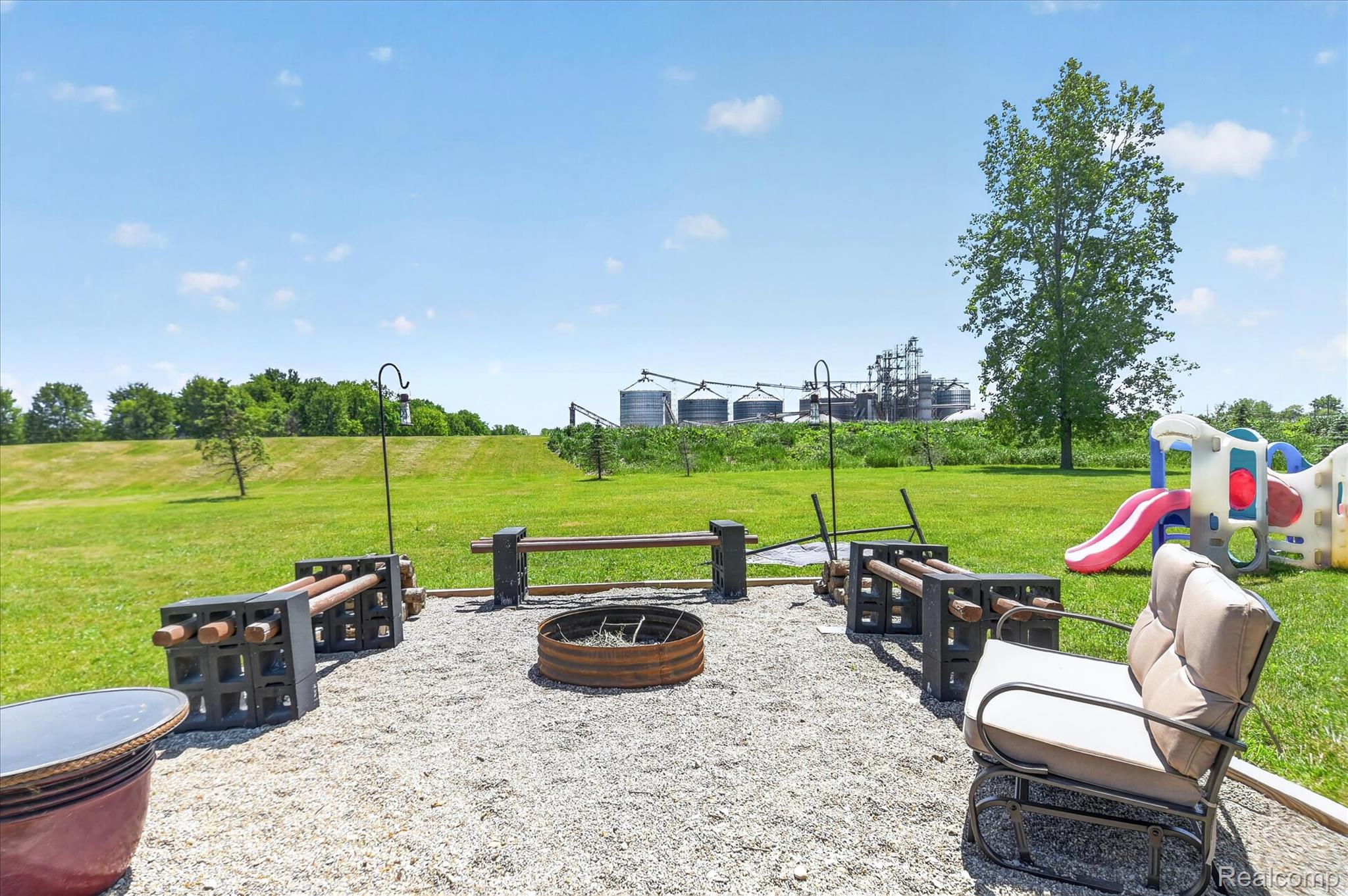 3949 West Burns Line Road Brown City, MI 48416 - Photo 66 of 70 Gravel patio area featuring a metal fire pit and built-in seating constructed from concrete blocks and wooden beams