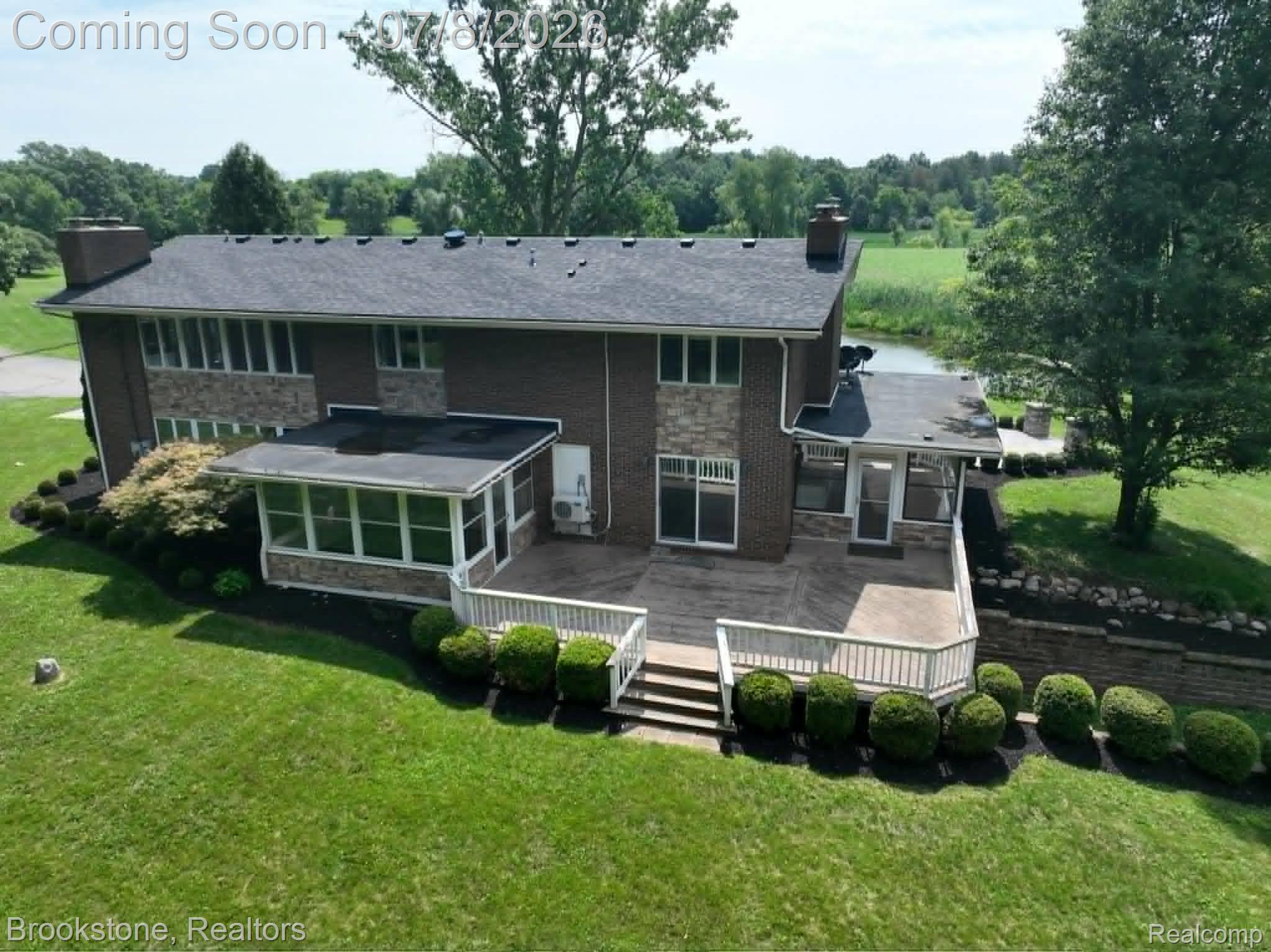 4140 South Henderson Road Davison, MI 48423 - Photo 4 of 98 Multi-level rear exterior featuring brick and stone veneer, a screened porch, and an expansive stamped concrete patio with a deck overlooking a natural water feature