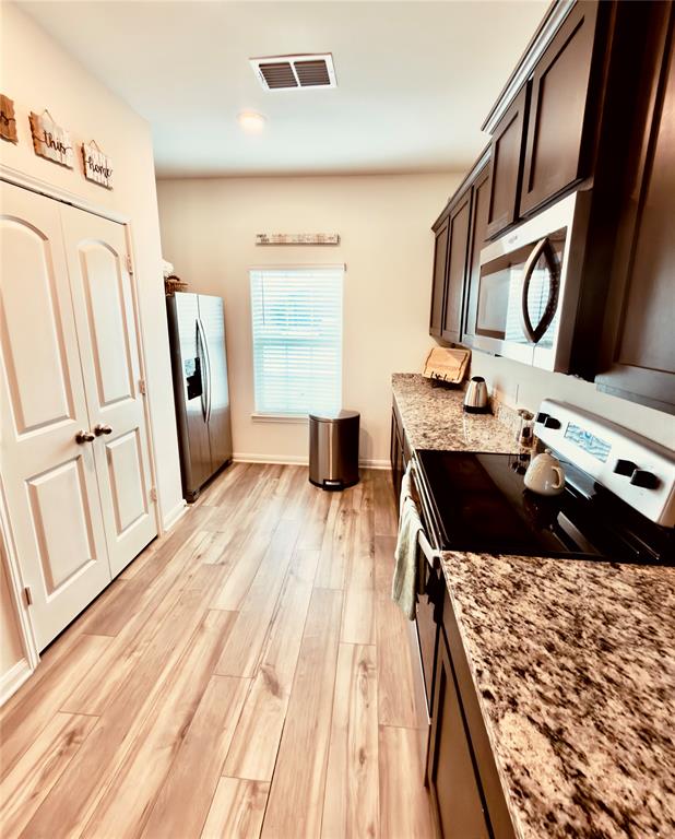 196 Cattlemans Crk Road West Newark, TX 76071 - Photo 2 of 24 Galley kitchen featuring wood-finish flooring, dark wood cabinetry, and speckled countertops