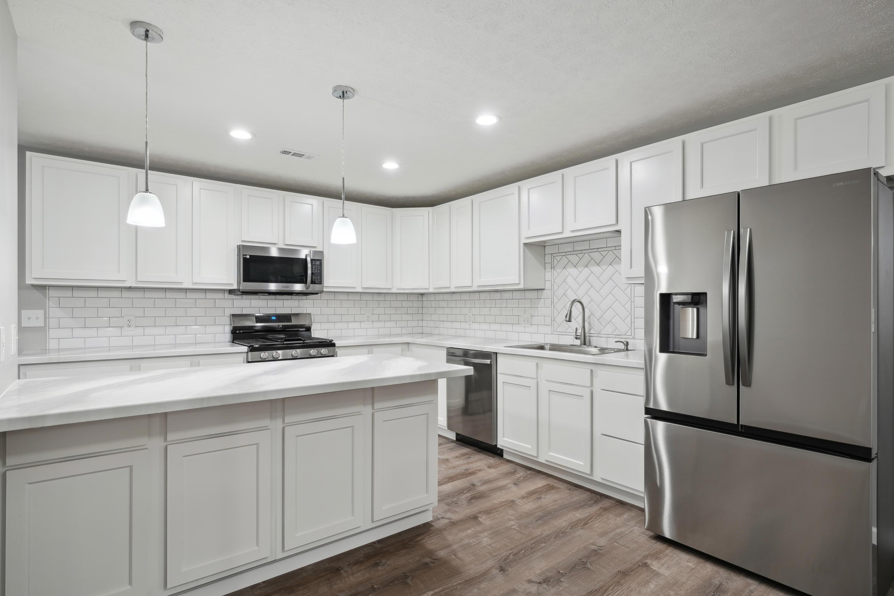 6705 Johnson Road Galloway, OH 43119 - Photo 9 of 30 Kitchen features white cabinetry, subway tile backsplash, stainless steel appliances, including a gas range, plus single basin sink, countertop seating with pendant lighting and pantry!