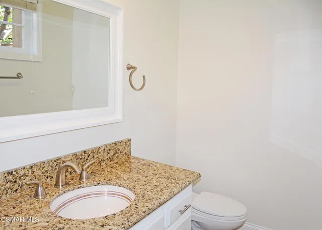 a bathroom with a granite countertop sink toilet and mirror