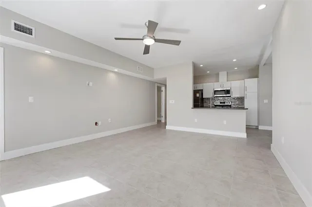 an empty room with a ceiling fan and kitchen view