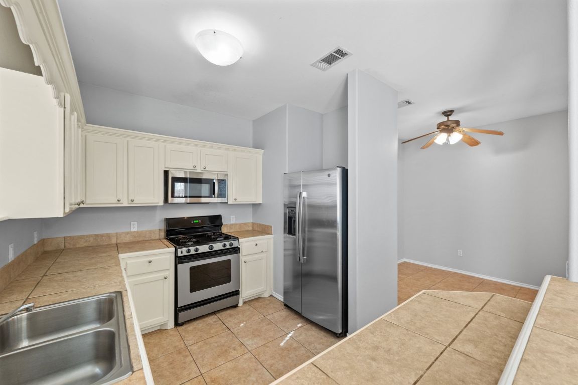 2906 Pearl Street, Unit B Austin, TX 78705 - Photo 12 of 30 Kitchen with appliances with stainless steel finishes, light tile patterned flooring, ceiling fan, tile counters, and white cabinets
