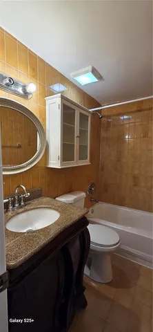 a bathroom with a granite countertop sink a toilet a mirror and bathtub