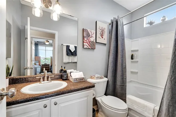 a bathroom with a granite countertop toilet a sink a mirror a vanity and shower