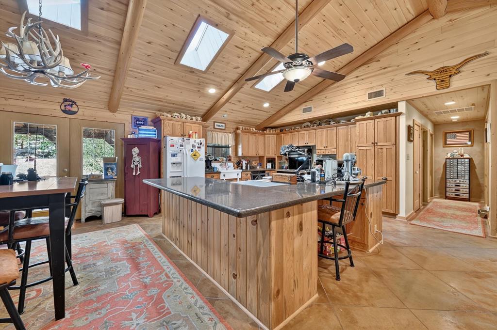 1623 3 Skillet Road Springtown, TX 76082 - Photo 15 of 40 Kitchen featuring a vaulted wood-paneled ceiling, exposed wood beams, skylights, wood cabinetry, and a substantial island with a dark countertop