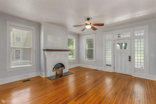 a view of a livingroom with a fireplace a ceiling fan and wooden floor