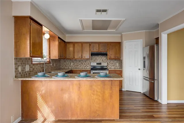 a kitchen with stainless steel appliances granite countertop a refrigerator a sink dishwasher a stove and white countertops with wooden floor