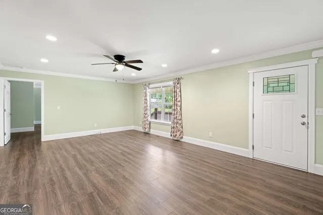 a view of an empty room with wooden floor and a ceiling fan