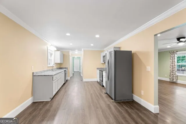 a large kitchen with a refrigerator a sink dishwasher a stove and white cabinets with wooden floor