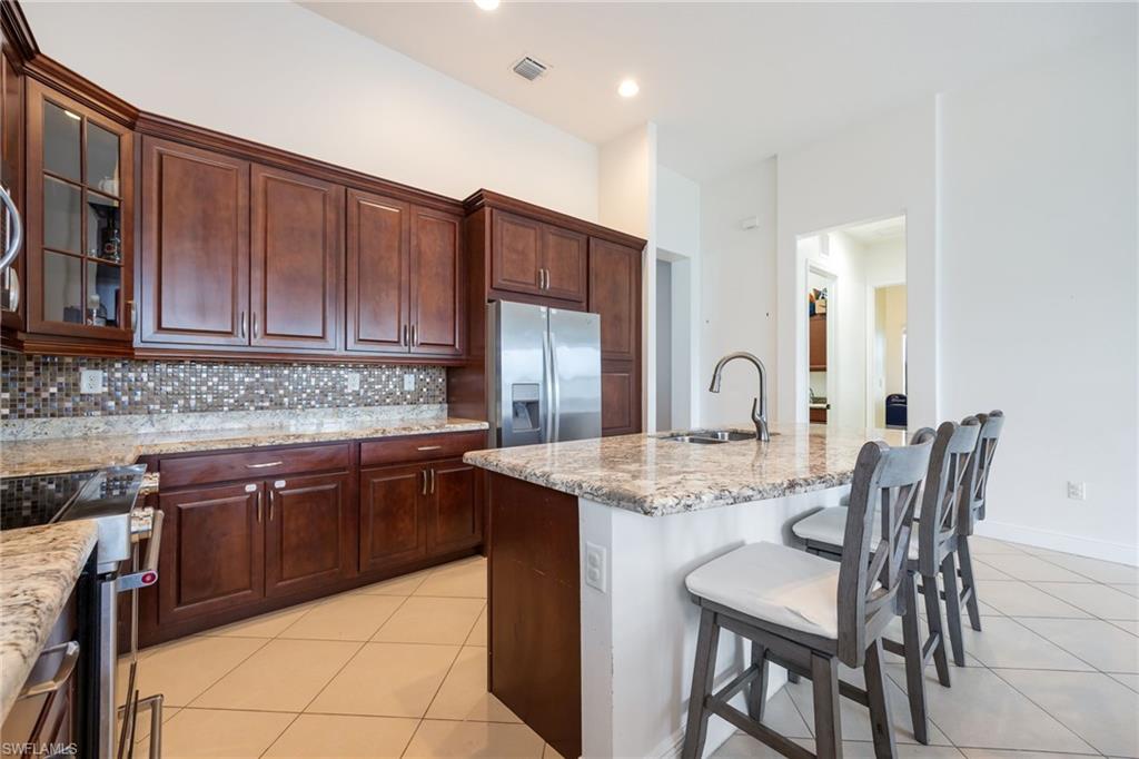5116 Salerno Street Ave Maria, FL 34142 - Photo 10 of 36 Kitchen with light tile patterned floors, a breakfast bar, glass insert cabinets, and stainless steel appliances