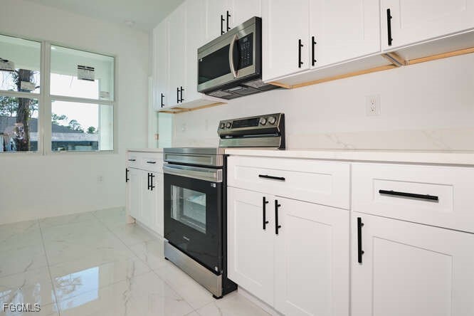3421 55th Street West Lehigh Acres, FL 33971 - Photo 15 of 38 a kitchen with stainless steel appliances granite countertop white cabinets and black appliances