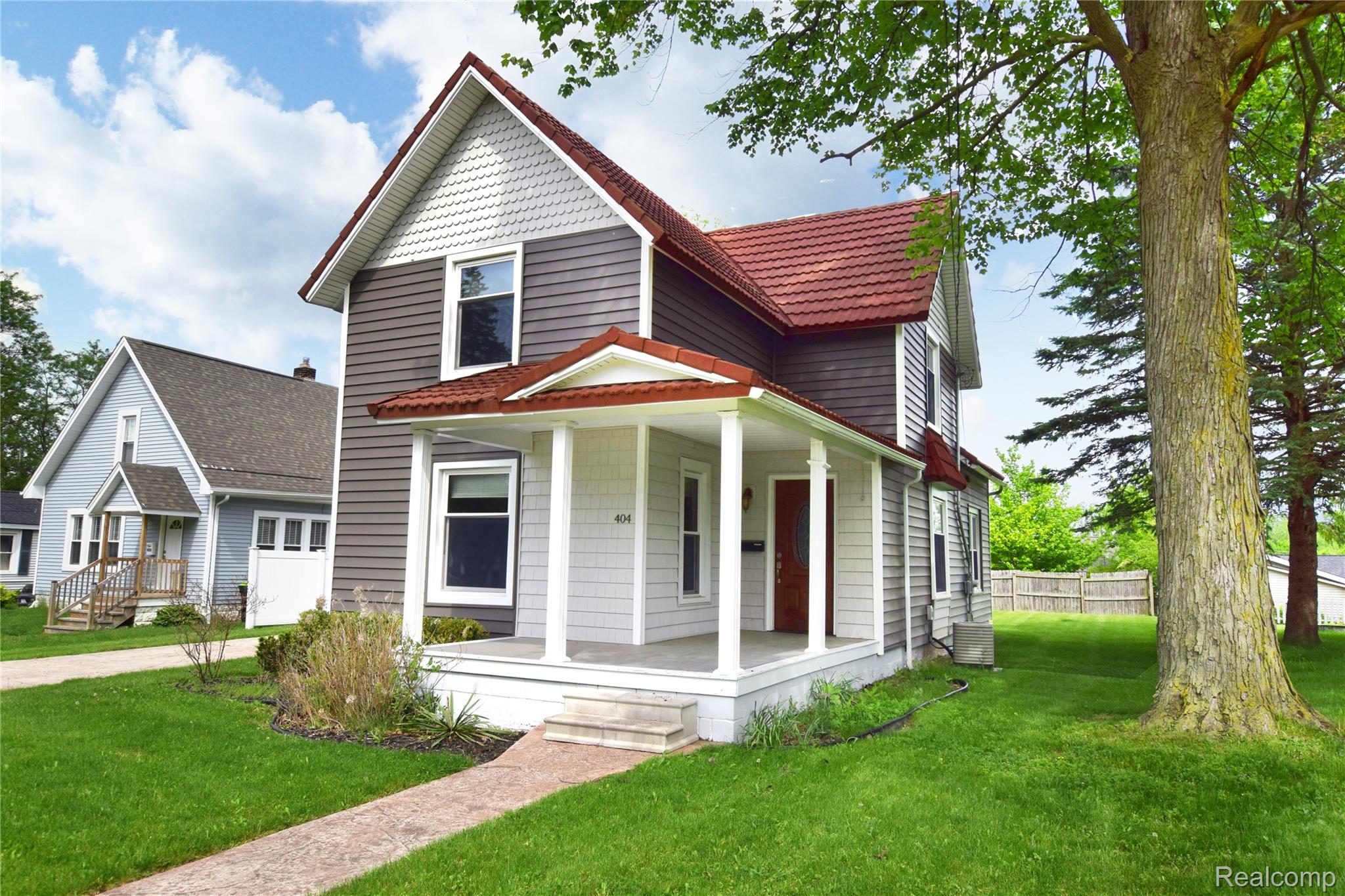 404 North Adelaide Street Fenton, MI 48430 - Photo 2 of 23 Two-story residence featuring a covered front porch with white columns, a red entry door, and a combination of horizontal siding and decorative shingles