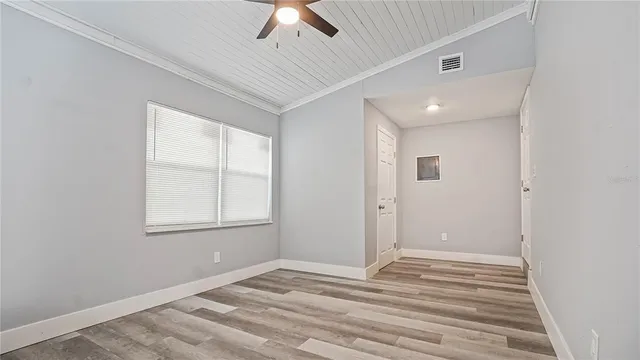 an empty room with wooden floor chandelier fan and windows