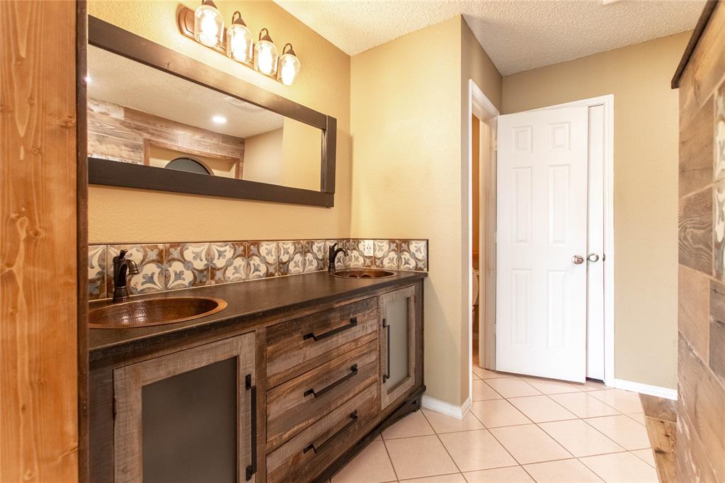 308 Sanders Road Denton, TX 76210 - Photo 4 of 31 Wood-finish vanity with dual copper vessel sinks, patterned tile backsplash, and a contemporary light fixture