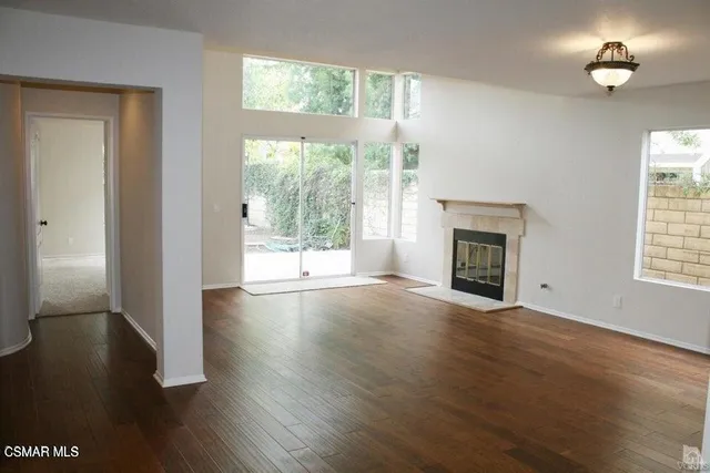 an empty room with wooden floor fireplace and windows