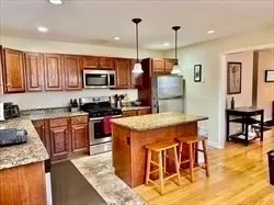 a kitchen with stainless steel appliances granite countertop a stove top oven a sink a dining table and chairs with wooden floor
