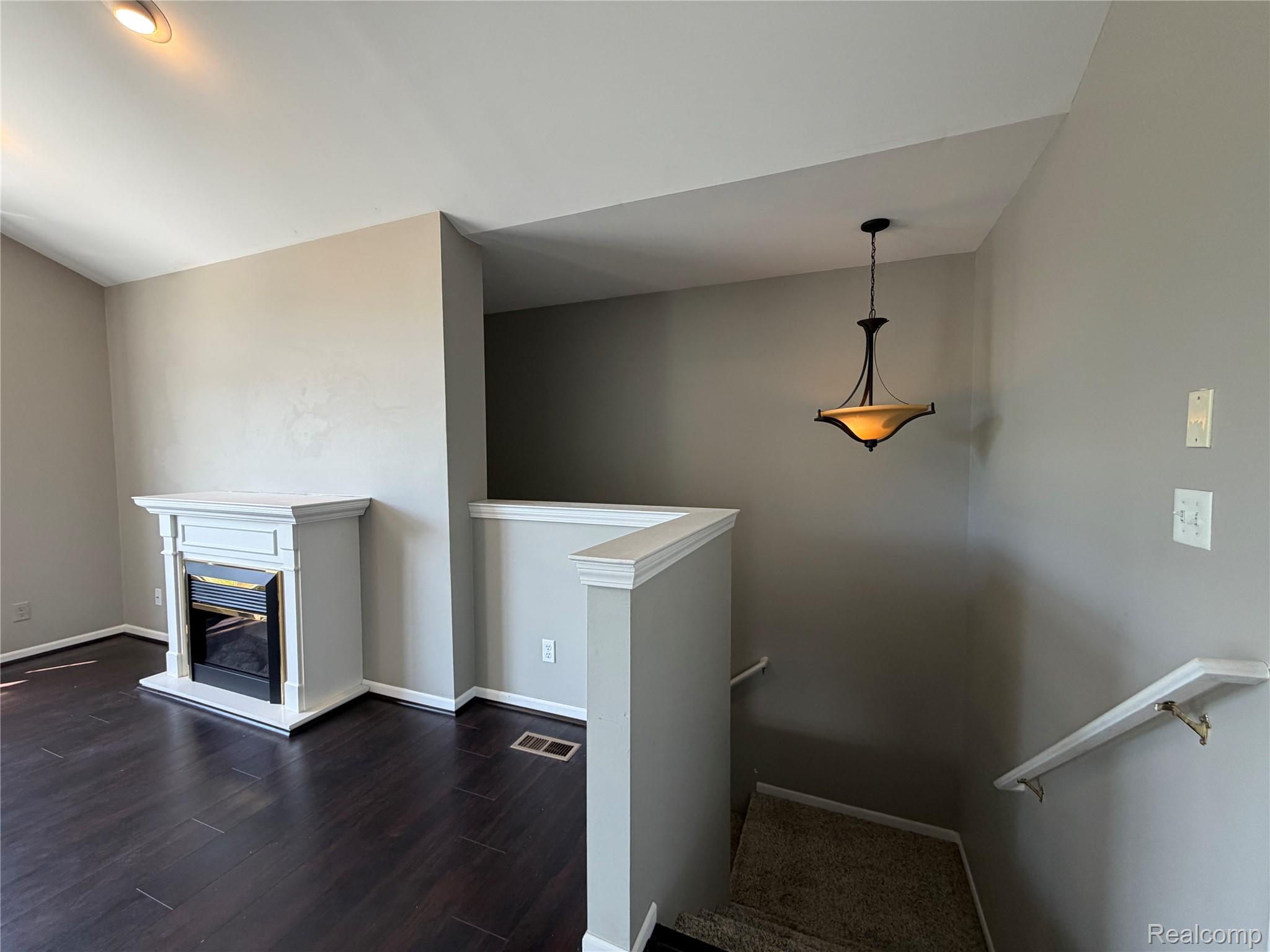 1908 Flagstone Circle Rochester, MI 48307 - Photo 4 of 25 Living area featuring a fireplace with a white mantel, dark wood-finish flooring, recessed lighting, and a pendant light fixture illuminating the stairwell with carpeted steps