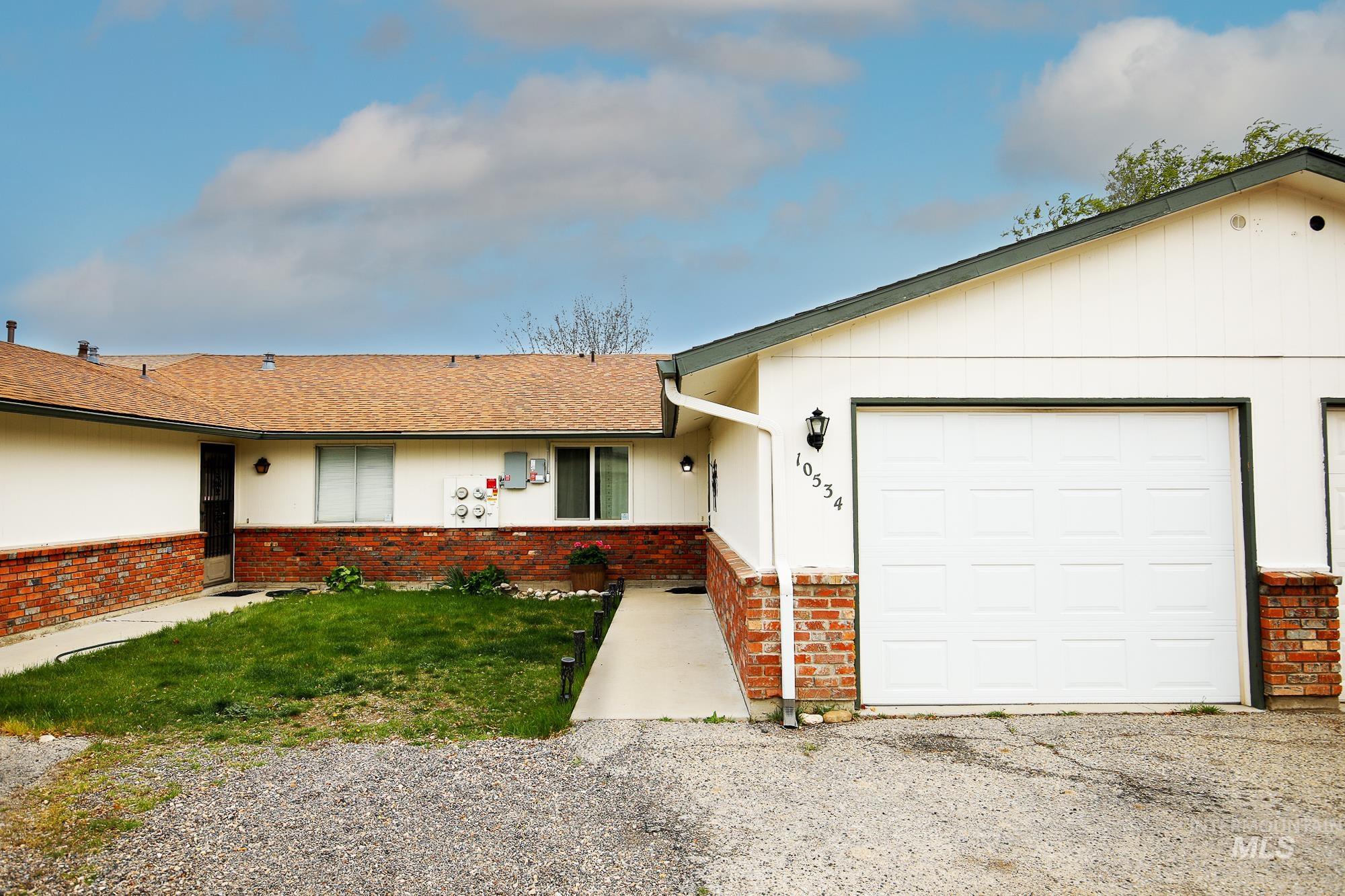 Single story home featuring a garage, brick siding, roof with shingles, and driveway