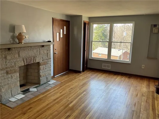 a view of an empty room with wooden floor fireplace and a window