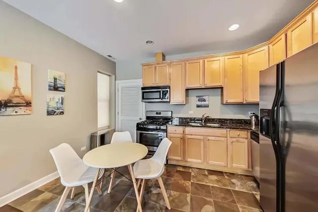 a kitchen with stainless steel appliances granite countertop a stove a refrigerator a sink a dining table and chairs with wooden floor