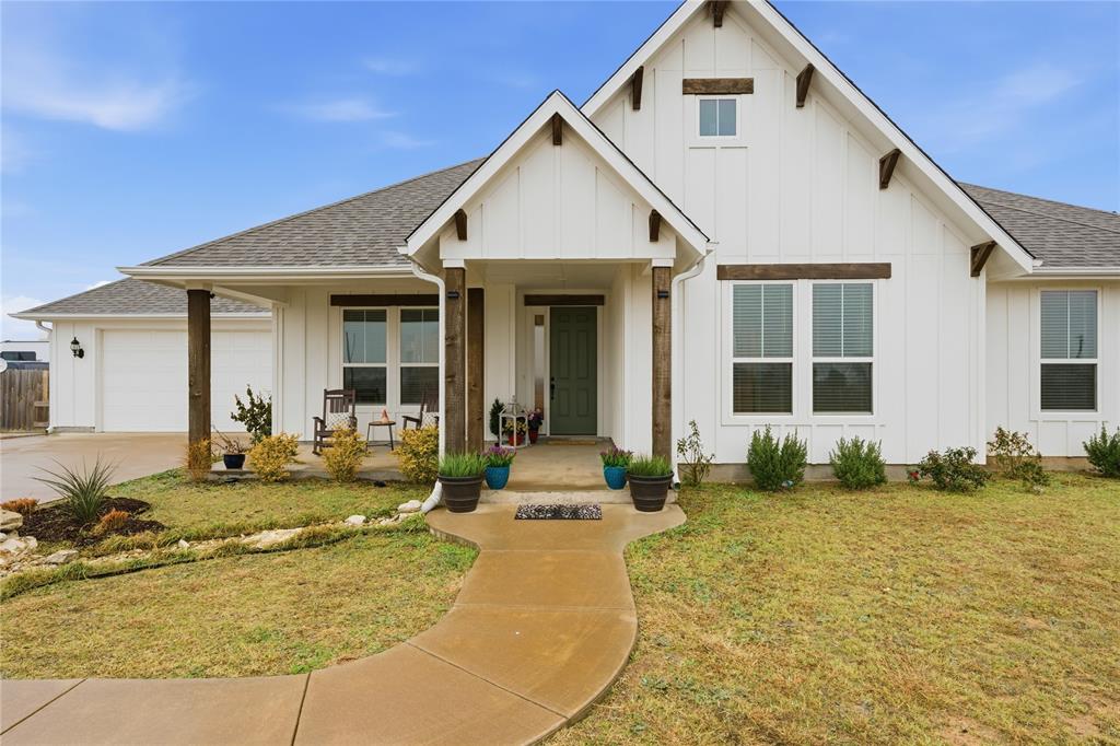 1292 Whiskey Hollow Road West, TX 76691 - Photo 3 of 34 View of front of property with board and batten siding, a front lawn, a shingled roof, a porch, and concrete driveway