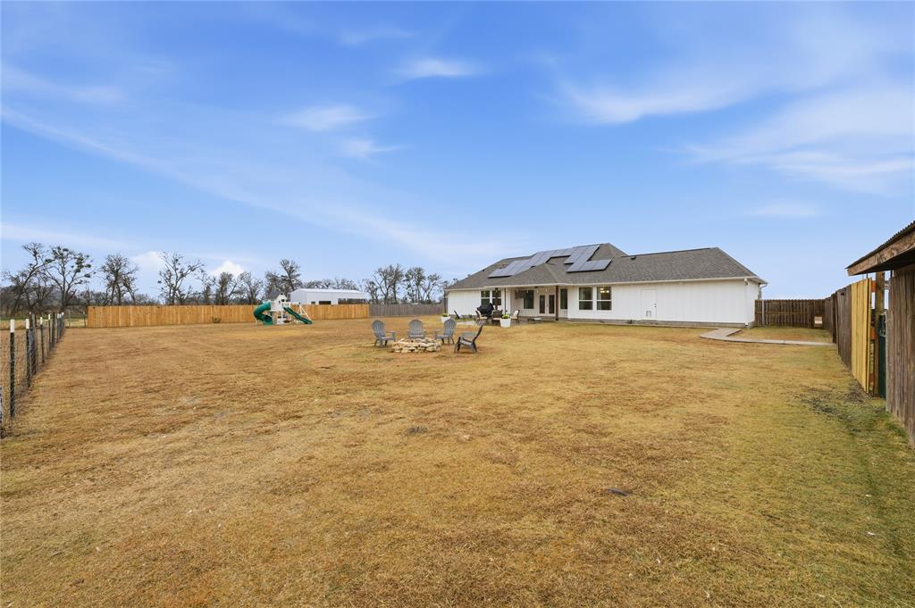 1292 Whiskey Hollow Road West, TX 76691 - Photo 33 of 34 Back of house featuring roof mounted solar panels, a fenced backyard, a patio area, a playground, and an outdoor fire pit