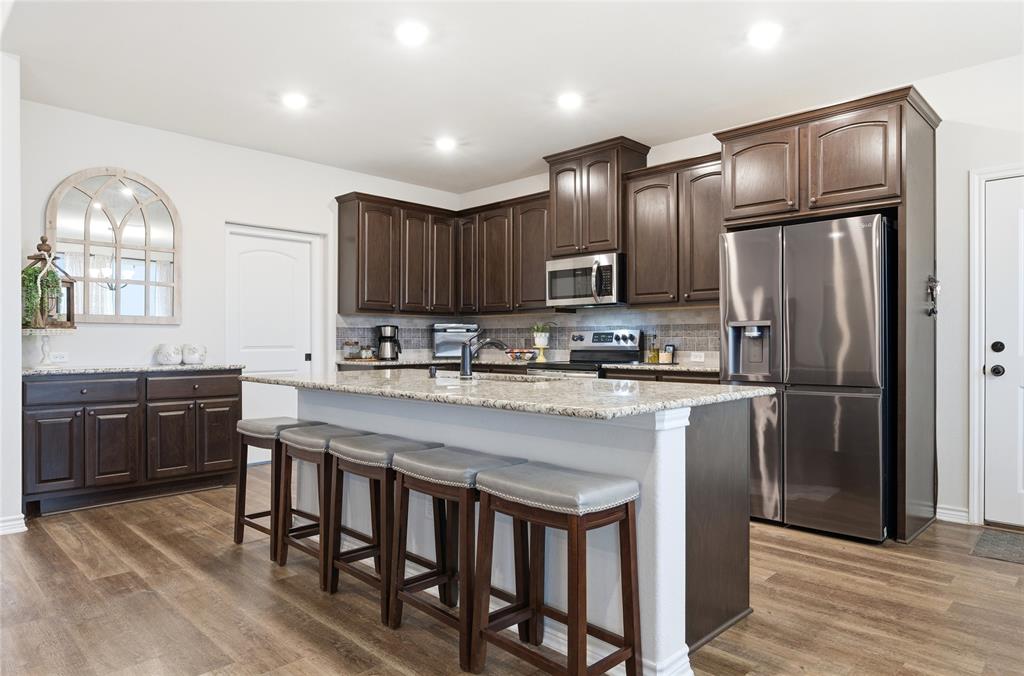 1292 Whiskey Hollow Road West, TX 76691 - Photo 9 of 34 Kitchen featuring stainless steel appliances, dark brown cabinetry, light stone countertops, a kitchen bar, and dark wood finished floors