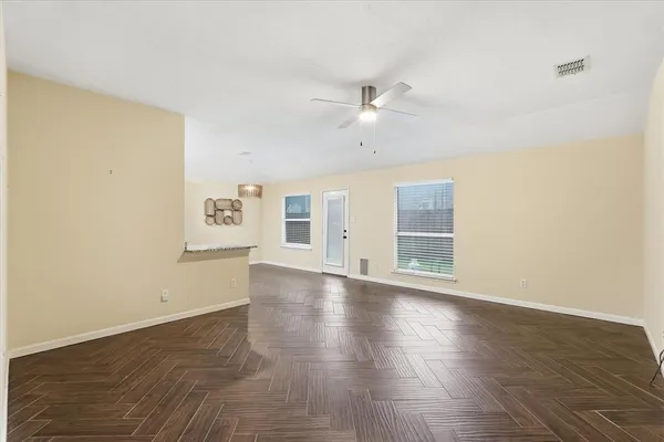 an empty room with wooden floor fan and windows
