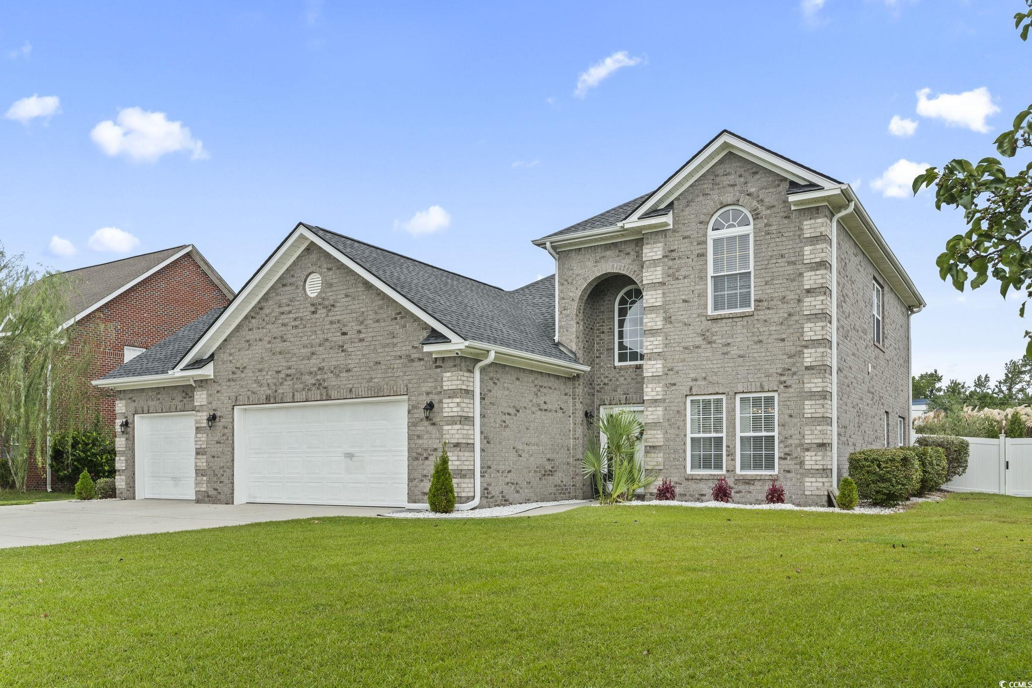 Traditional-style house with brick siding, a front yard, driveway, and an attached garage