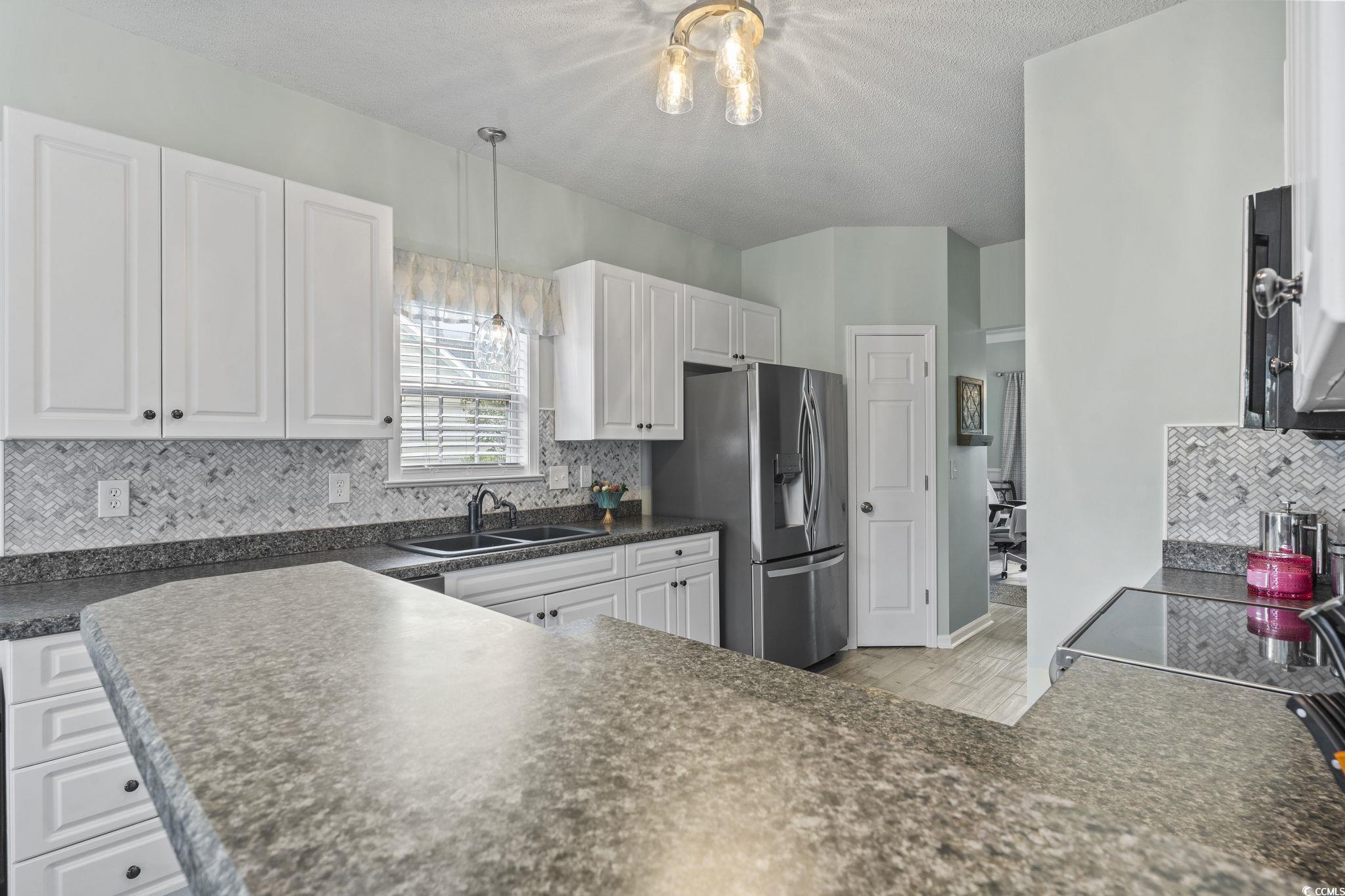 212 Duchess Court Myrtle Beach, SC 29588 - Photo 7 of 40 Kitchen with dark countertops, decorative backsplash, white cabinets, stainless steel fridge with ice dispenser, and decorative light fixtures