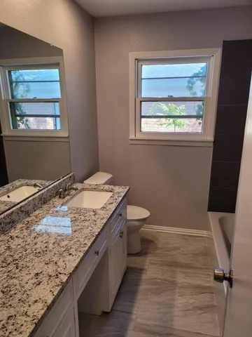 a bathroom with a granite countertop double vanity sink a mirror and a toilet