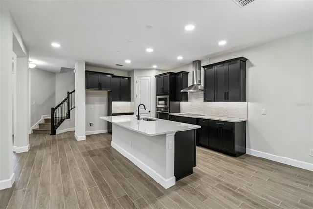 a large kitchen with stainless steel appliances kitchen island a large counter top a sink wooden floor and living room view