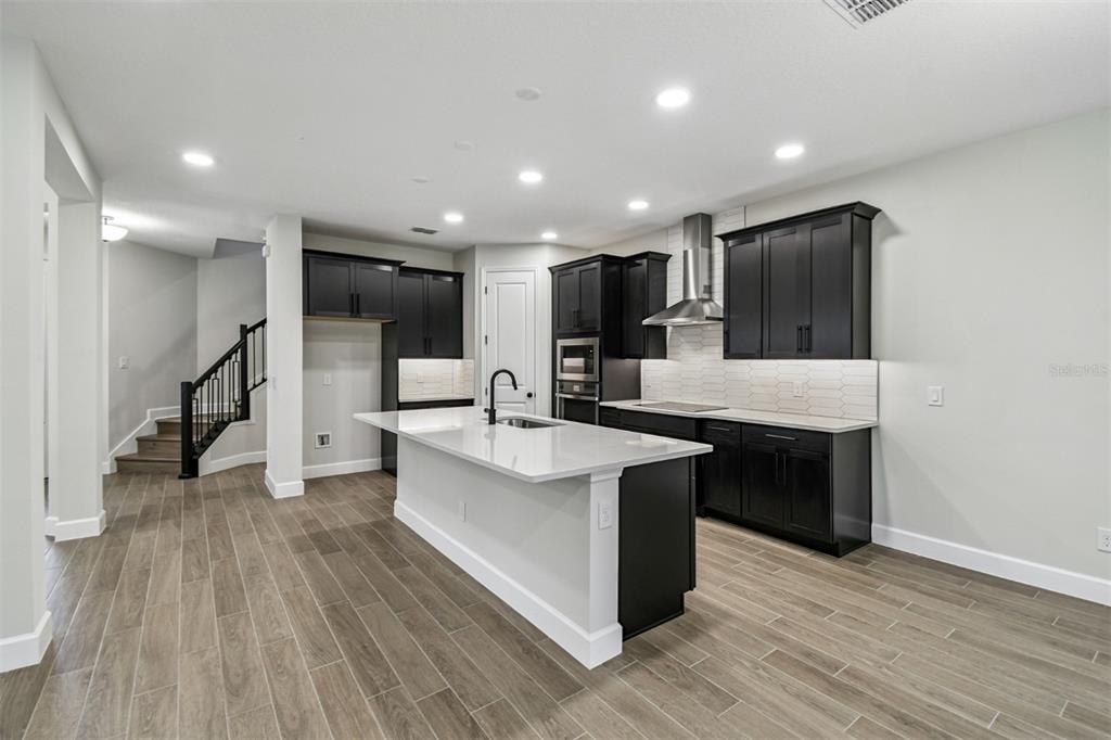 5262 Prairie Preserve Run St. Cloud, FL 34772 - Photo 5 of 40 a large kitchen with stainless steel appliances kitchen island a large counter top a sink wooden floor and living room view
