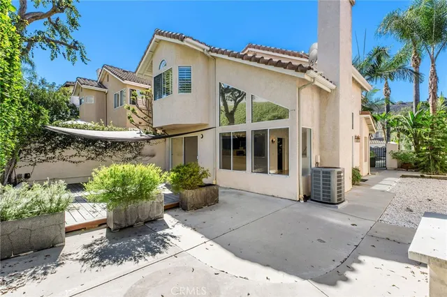 a view of a white house with potted plants and a large tree