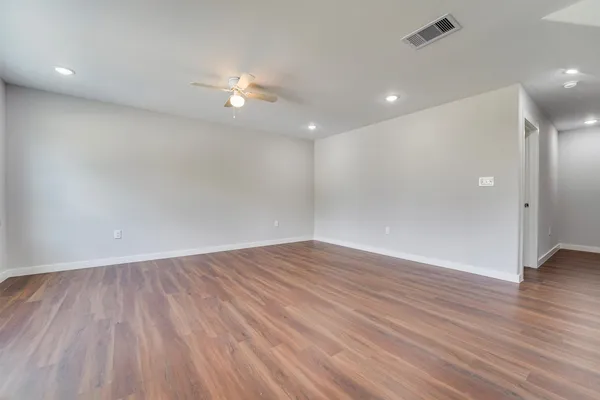 a view of an empty room with wooden floor and a ceiling fan