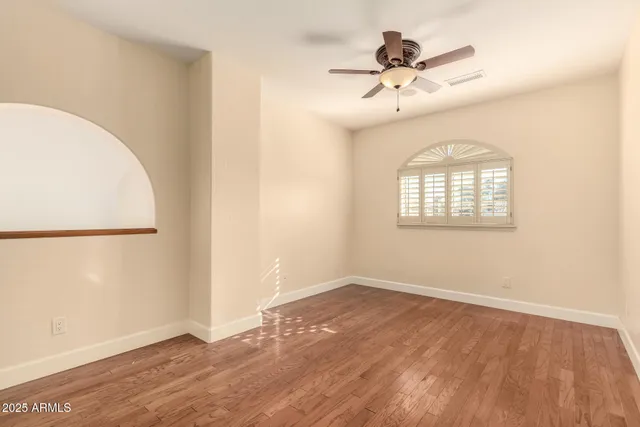 an empty room with wooden floor fan and windows