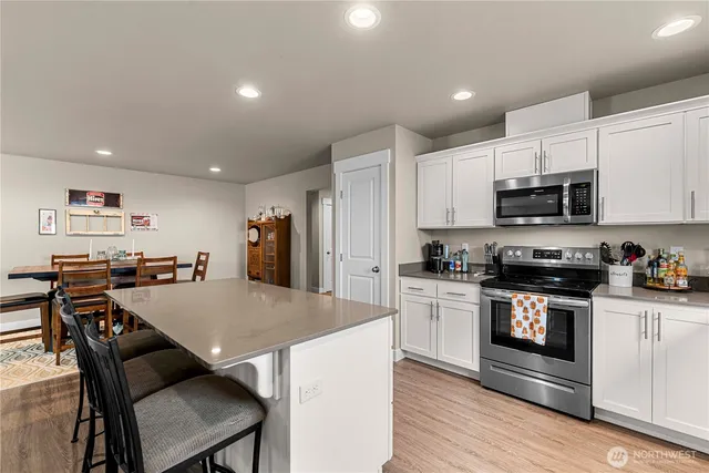 a kitchen with stainless steel appliances a stove a sink a microwave a refrigerator white cabinets and wooden floor