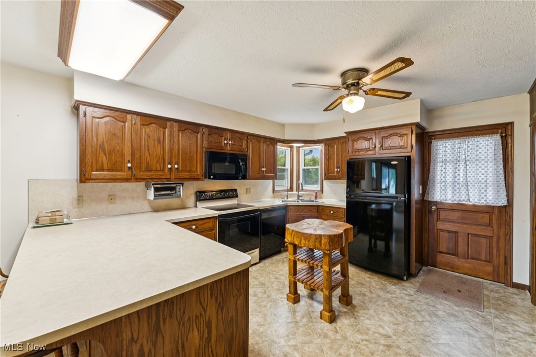 12422 Portage Street Rittman, OH 44270 - Photo 12 of 42 Kitchen with light countertops, black appliances, a peninsula, brown cabinets, and a textured ceiling