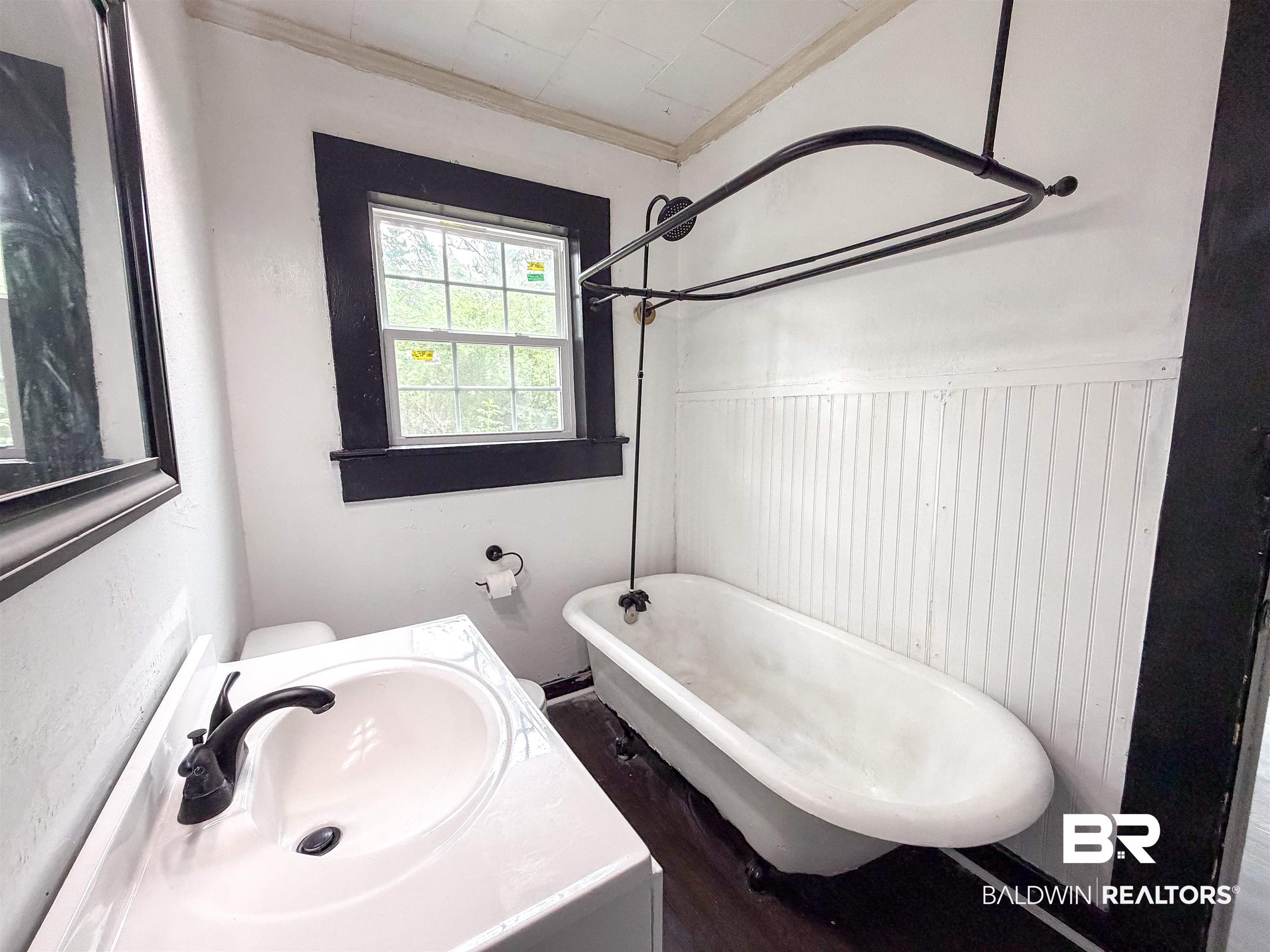 38 Flock Avenue Mobile, AL 36610 - Photo 16 of 27 Bathroom featuring a white clawfoot tub with a matte black shower curtain rod, white beadboard wainscoting, a white vanity with an integrated sink, and dark bronze fixtures