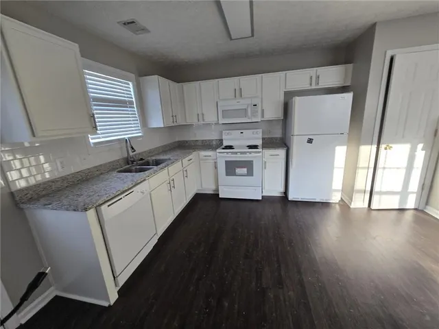 a kitchen with stainless steel appliances a sink dishwasher a refrigerator a stove and white cabinets with wooden floor